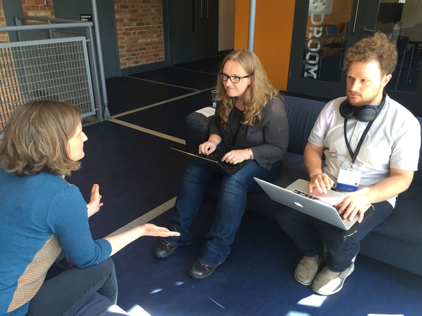 Three participants sat on sofas with laptops and in discussion