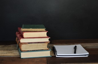 Stack of books next to a notepad and pen