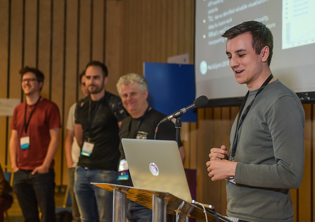 The development team stand at a microphone for a presentation