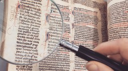 Magnifying glass held over ancient manuscript