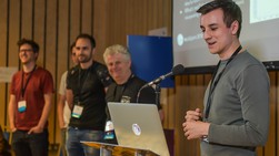 The development team stand at a microphone for a presentation