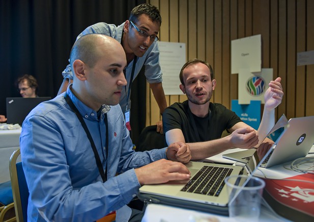 Three people lean over laptops to discuss work
