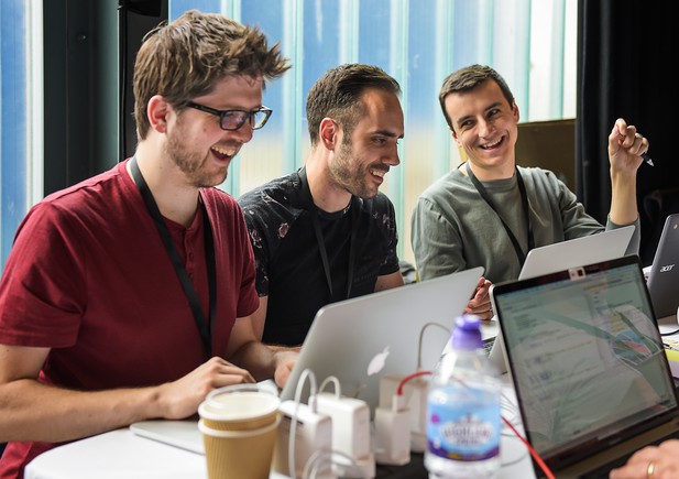 Three people laugh as they sit working on laptops